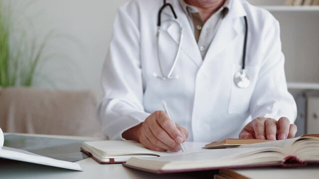 Doctor study. Medical science. Professional research. Unrecognizable male physician working with books reading taking notes at modern workplace interior.