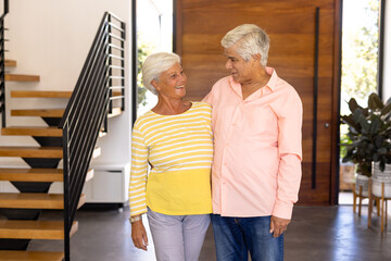 Smiling biracial senior friends looking at each other while standing against door in nursing home