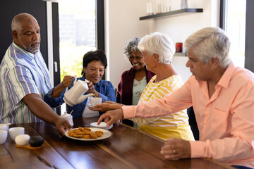 Multiracial happy senior male and female friends enjoying coffee and cookies in nursing home