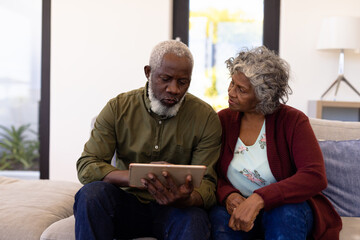 African american senior man using digital tablet while sitting with woman on sofa in nursing home - Powered by Adobe