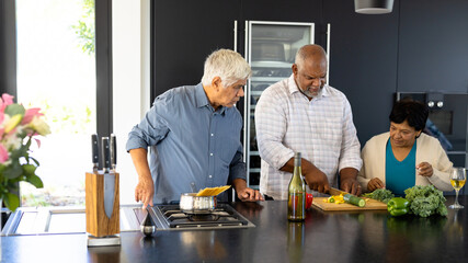 Biracial senior friends looking at man chopping vegetables on kitchen island in nursing home
