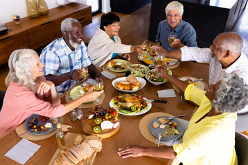 High angle view of multiracial senior friends toasting wineglasses at dining table in nursing home
