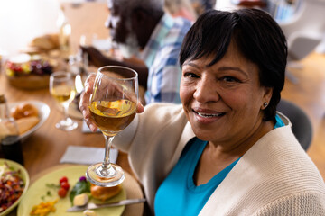 Portrait of multiracial senior woman enjoying wine while having lunch with friend at dining table