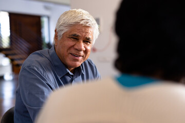 Smiling biracial senior man talking with female friend while sitting for lunch in nursing home - Powered by Adobe