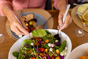 Cropped hands of caucasian senior woman taking vegetable salad with spoons on dining table