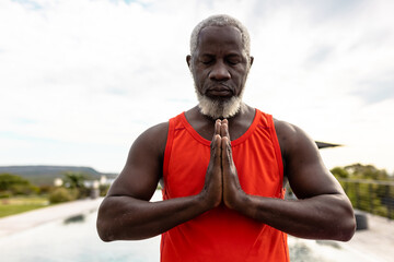African american senior man with eyes closed meditating in prayer position against sky in yard © WavebreakMediaMicro