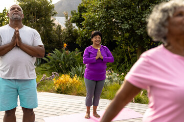 Multiracial senior friends with eyes closed meditating against plants in yard at nursing home