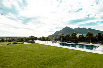 Fototapeta na wymiar Scenic view of grassy land and swimming pool against mountain and cloudy sky