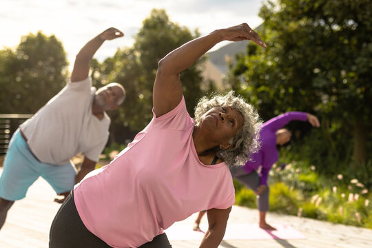 Multiracial senior friends practicing yoga against plants in yard during summer