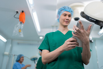 Fototapeta na wymiar Portrait of Asian surgeon with medical mask standing and holding a tablet in operation theater at a hospital. Team of Professional surgeons. Healthcare, emergency medical service concept