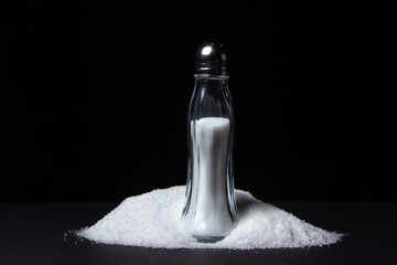 Salt shaker on a pile of salt on a black background. Excessive salt intake. food salt