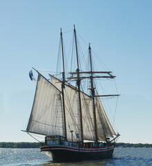 Fototapeta premium Wooden sail ship in backlight with rope shadows projected to the white sails travelling to the quite calm sea in a sunny weather. 