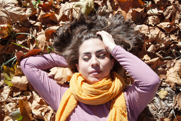 Chica relajada tirada entre hojas en otoño.