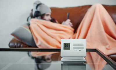 Power crisis. Cold home, close up of indoor thermometer with low temperature. Freezing teenager in...