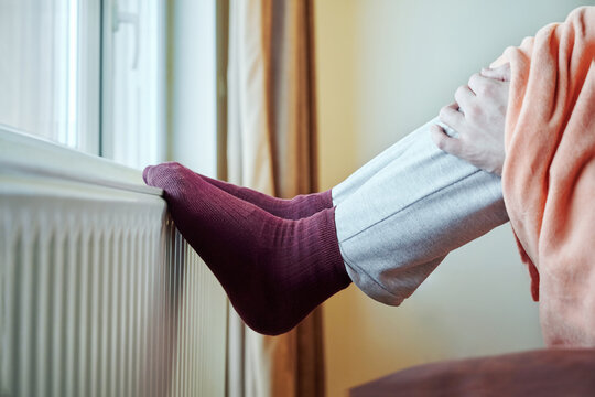 Male legs wearing warm socks on heating radiator is trying to warm up . Power crisis concept, problem with heating