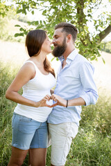 pretty young pregnant woman with white shirt stands with her boyfriend with beard and blue shirt in high flower meadow and cuddle