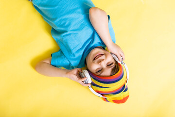 cute little boy in blue shirt and colorful hat with headphones, yellow background, upside down