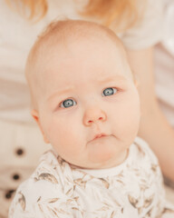 Portrait of wonderful serious grey-eyed plump cherubic baby infant toddler wearing beige bodysuit with patterns sitting.