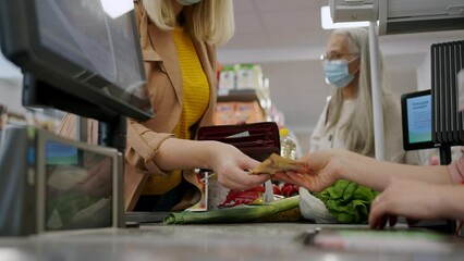Close-up of woman giving money at the cash desk in supermarket during pandemic.