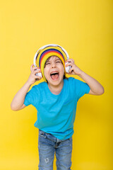 Handsome little boy in blue shirt and colorful hat with headphones, yellow background
