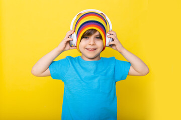 Handsome little boy in blue shirt and colorful hat with headphones, yellow background