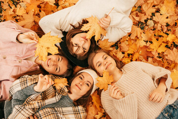 Autumn portrait of Happy four young women students playing with leaves, smiling while lying on ground in park, top view