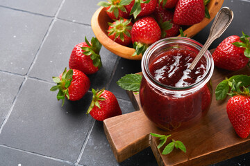 Strawberry jam. Strawberry jam in glass jar with fresh berries plate on an old black cracked tile table background, closeup. Homemade strawberry fruity jam. Top view with copy space.