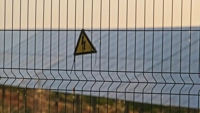 High voltage sign on a wire fence of the solar plant. Yellow triangular sign lightning danger high voltage. Warning electricity safety symbol of the power plant. Sign of the danger of electric shock.