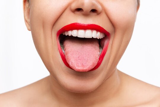 Cropped shot of young caucasian woman showing tongue with her mouth wide open isolated on a white background. Female lips with red lipstick. Teeth whitening. Oral hygiene, dental health care