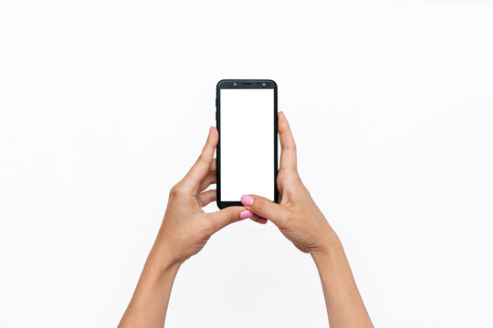 Mobile phone with white screen in female hands isolated on a white background. Blank with an empty copy space for the text. Template for the design. Mockup of a smartphone. A young woman takes picture
