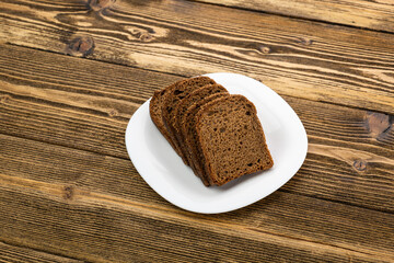 sliced rye bread in pieces in a white plate on a wooden background