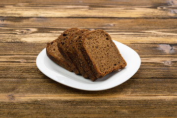 sliced rye bread in pieces in a white plate on a wooden background