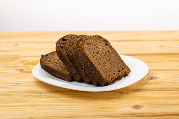 sliced rye bread in pieces in a white plate on a wooden background