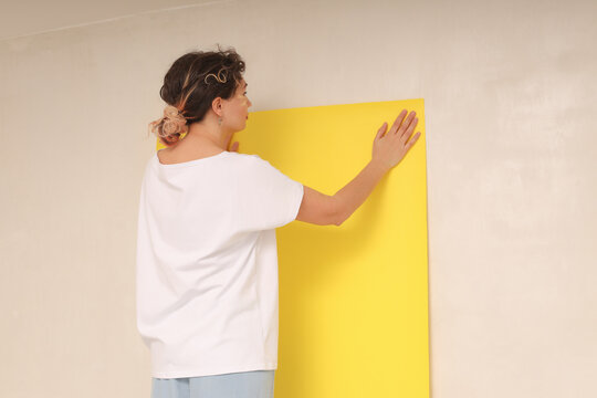 A woman glues yellow wallpaper on the wall