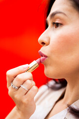 Young brunette woman using lipstick and against a red background