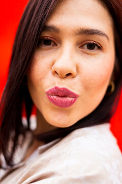 Portrait of a young brunette woman sending a kiss to the camera, against a red background