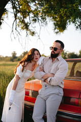 A young couple in love travels in a red retro car along a field road.