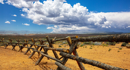 Log fence in a desert land, blue sky with clouds. Sunny spring day in American countryside, USA