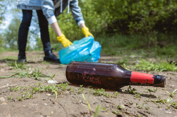 A woman picks up an abandoned glass bottle in the forest. Environmental garbage pollution