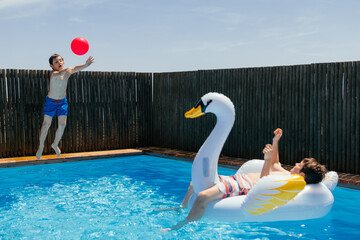 Boys playing ball and inflatable mattress in swimming pool