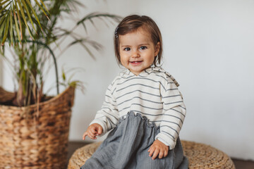 Pretty one year toddler girl in stripped dress posing in eco studio.