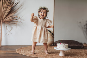 Girl in beige dress and flower crown posing with birthday cake in the studio