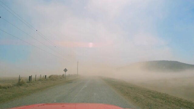 Driving through sandstorm as strong wind kicks up dirt in Idaho moving past farmers field next to the Menan Buttes.
