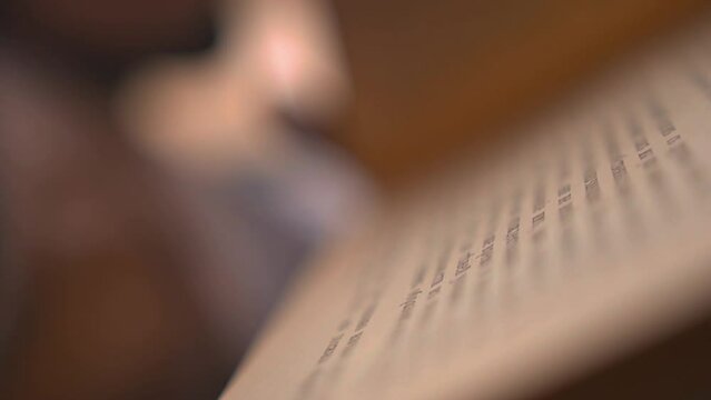 Young man flips the pages of a vintage book in a library. Guy touches aged book pages to feel the texture of a paper. Ancient volume of a rare edition of a book in an archive. Dissertation writing.