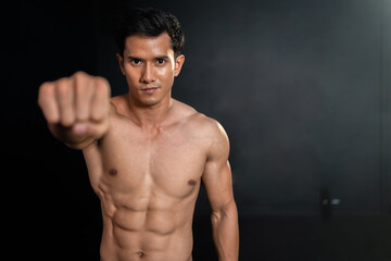 Asian strong muscular man clench fist showing six pack on black background in fitness gym.Sportsman...
