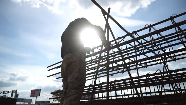 Welder in welding mask and welding gloves welds metal structure on construction site. Structural contractors erect supporting structures. Construction of modern high-rise buildings, city development.