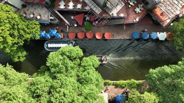 San Antonio TX famous River Walk. Aerial top down birds eye view of boats and barges passing by city restaurants in downtown.