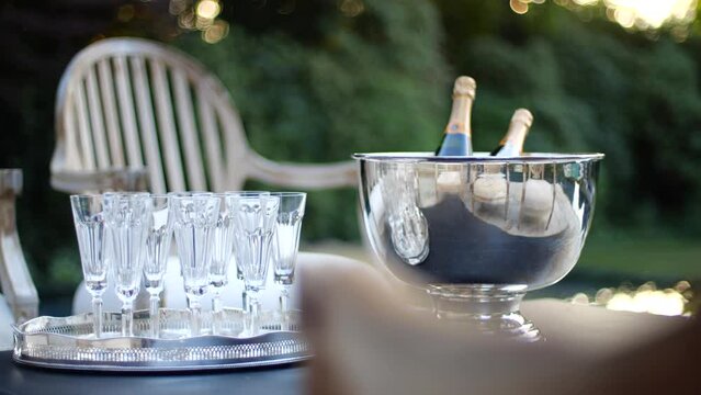 Two bottles of Veuve Clicquot champagne in silver bowl and ice in front of luxury home with glasses and chairs out for guests.