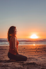 Fototapeta na wymiar middle-aged woman meditating in front of the sunrise sun on the sand of the beach
