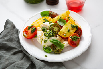 Close up of tomato and buratta chesese salad pesto dressing white plate